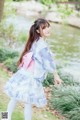 A woman in a blue and pink kimono standing next to a pond.