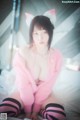 A woman in a pink cat costume sitting on a bed.