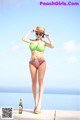 A woman in a bikini and hat standing next to a bottle of beer.