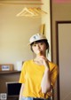 A woman in a yellow shirt and a white hat eating an ice cream cone.