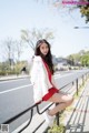 A woman in a red dress and white jacket sitting on a railing.