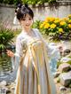 A woman in a white and yellow dress standing in front of a pond.