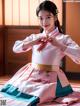 A woman in a pink and blue hanbok sitting on a bed.