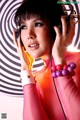 A woman in a pink outfit holding a pair of headphones.