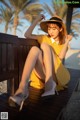 A woman in a yellow dress and hat sitting on a bench.